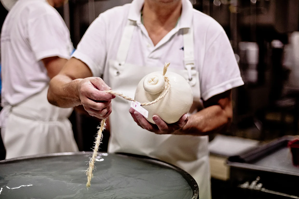 Mani al lavoro su una forma di pasta filata legata con lo spago